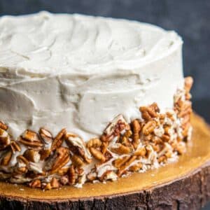 hummingbird cake with cream cheese frosting and crush pecans on the sides of the cake