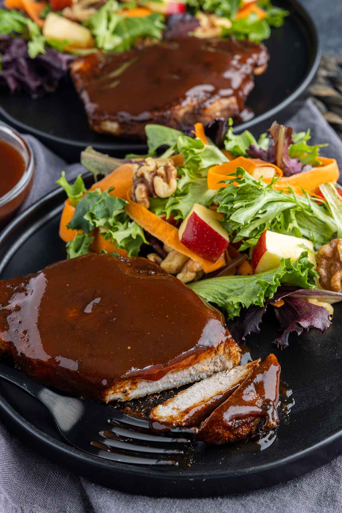 cut Air Fryer BBQ Pork Chops on a black plate with salad