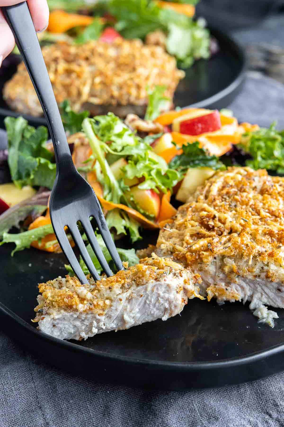 Air Fryer Parmesan Crusted Pork Chops on a black plate with a slice on a black fork