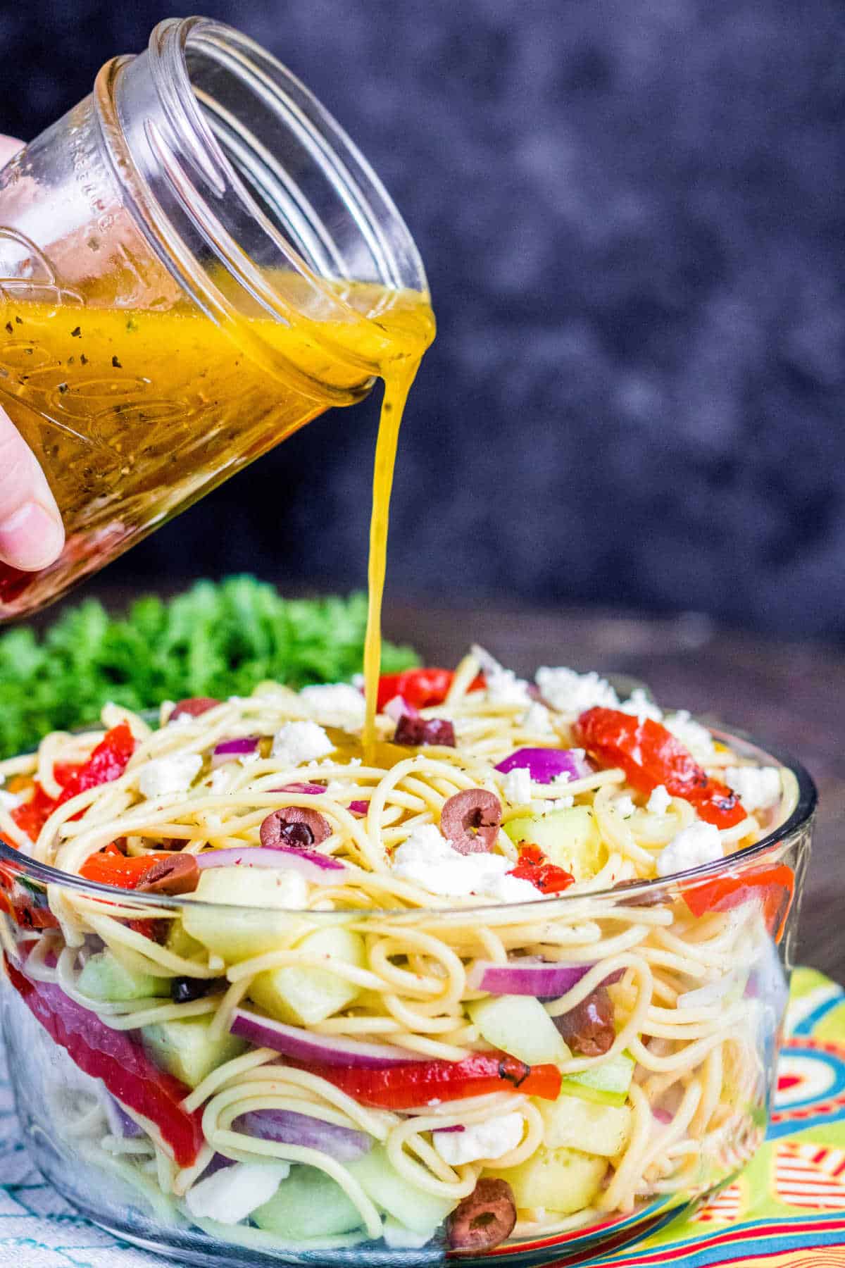 pouring dressing over Greek Spaghetti Salad