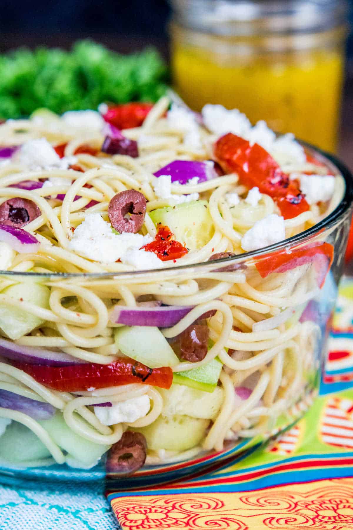 glass bowl with Greek Spaghetti Salad with jar of dressing behind bowl