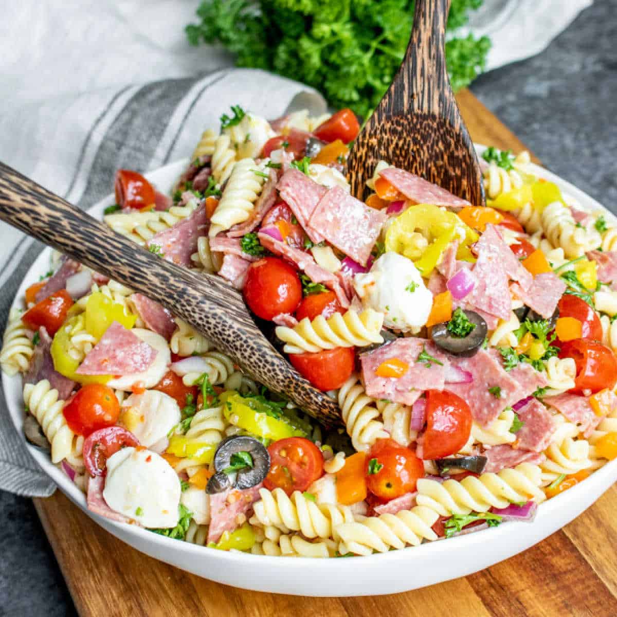 Italian Pasta Salad in a white bowl with wooden serving spoons