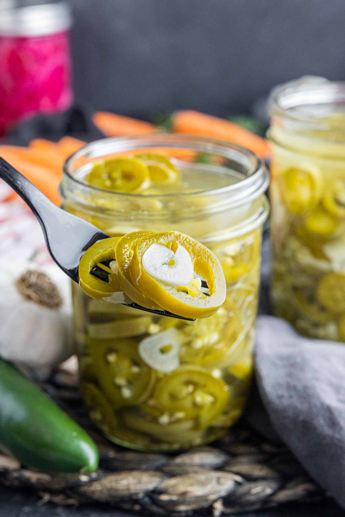 fork with Pickled Jalapenos on it with a jar of Pickled Jalapenos behind it