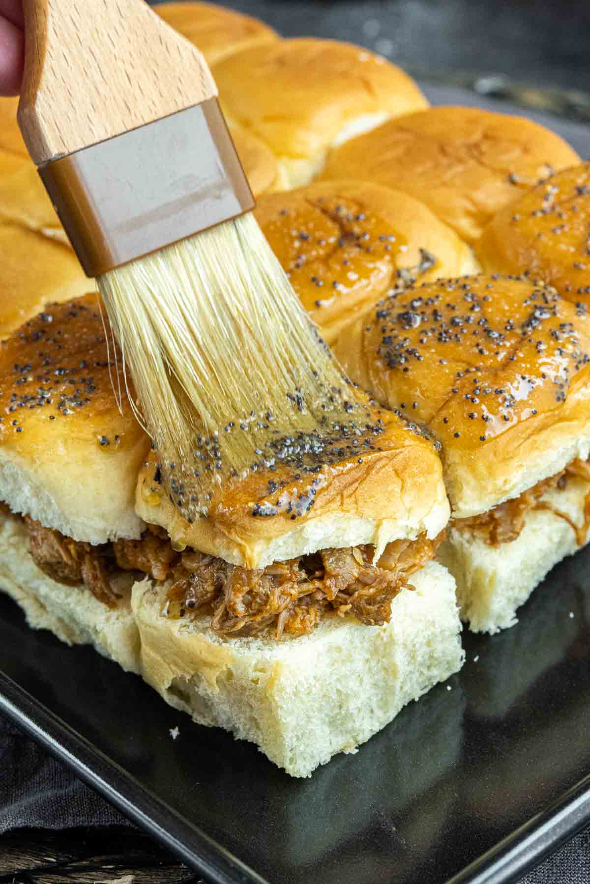 brushing poppy butter mixture on top of BBQ Pulled Pork Sliders