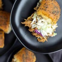 A plate of pulled pork sliders with coleslaw and sesame seeds.