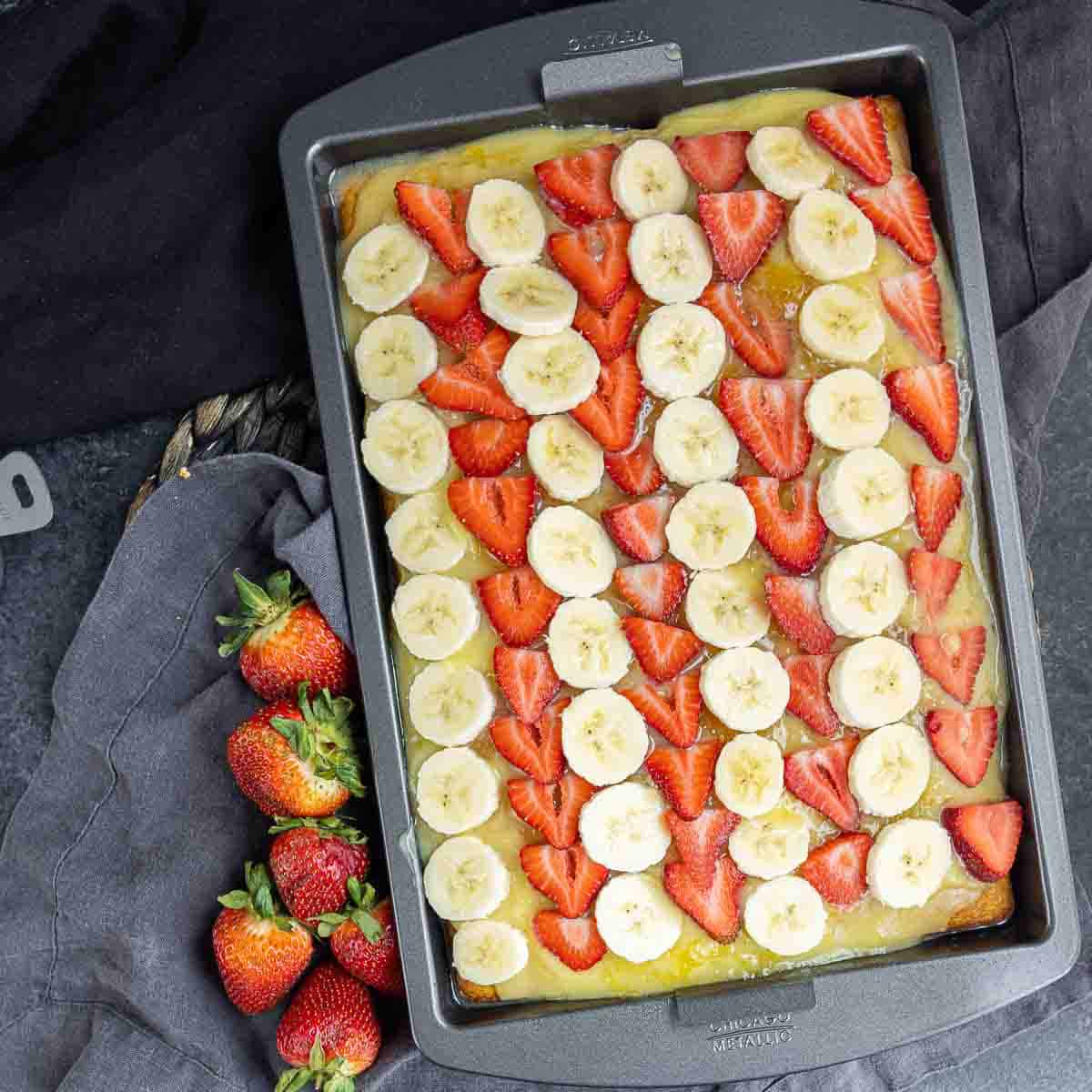 strawberries and banana sliced in rows on top of Banana Split Cake