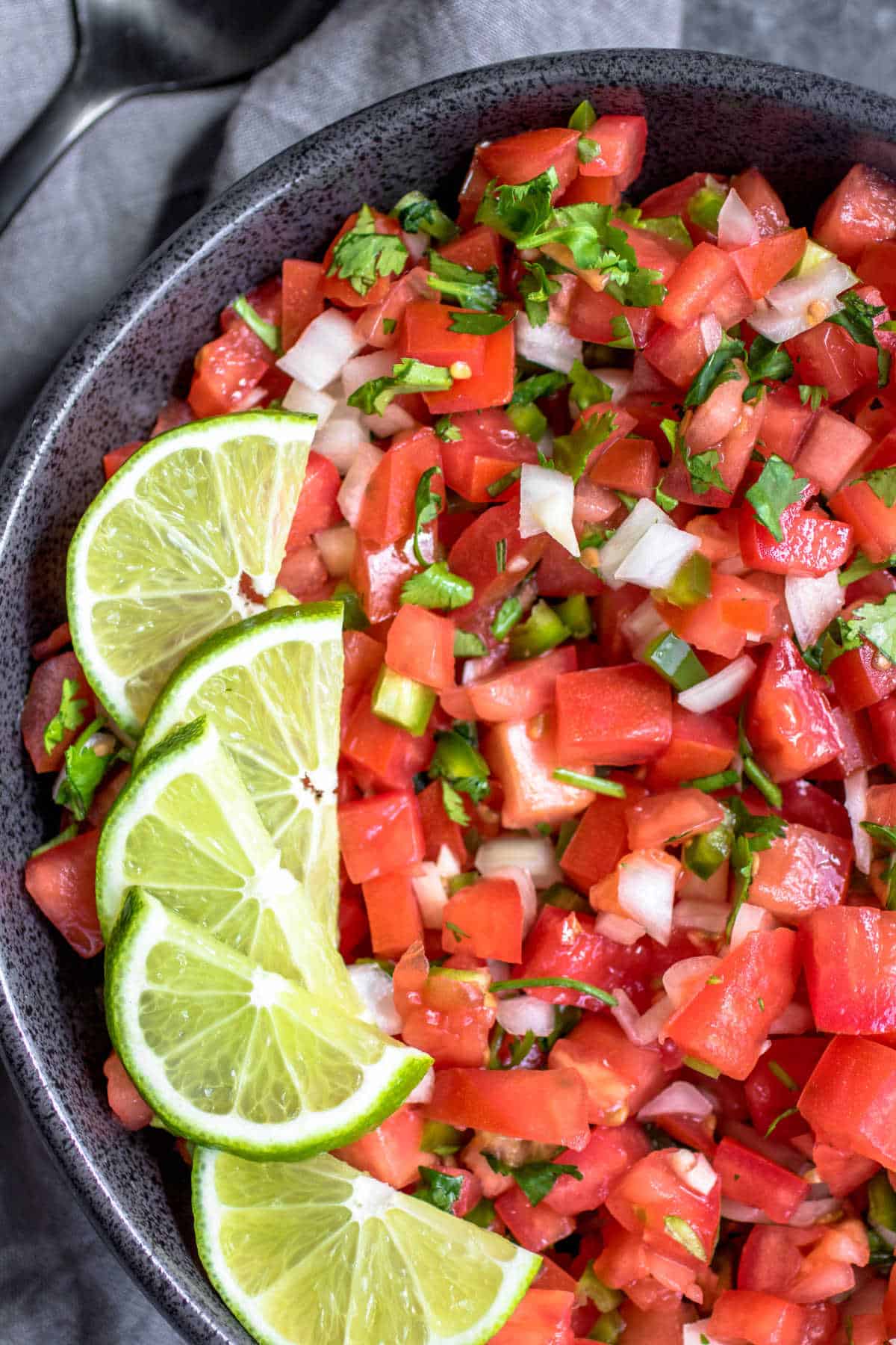 Fresh tomato salsa in a bowl with lime wedges on top as a garnish