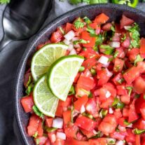 Salsa Fresca in a black bowl with three lime wedges