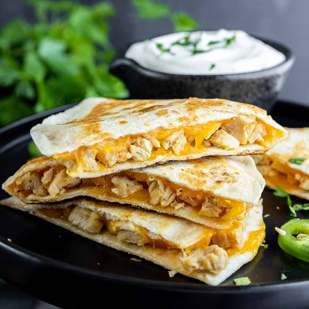 three stack ingredients to make Chicken Quesadillas on a black plate