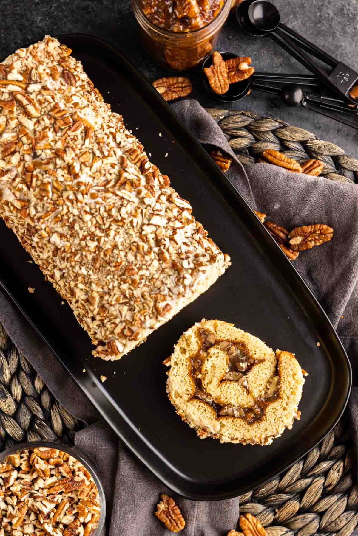 Pecan Pie Cake Roll on a platter with one slice and whole pecans scattered