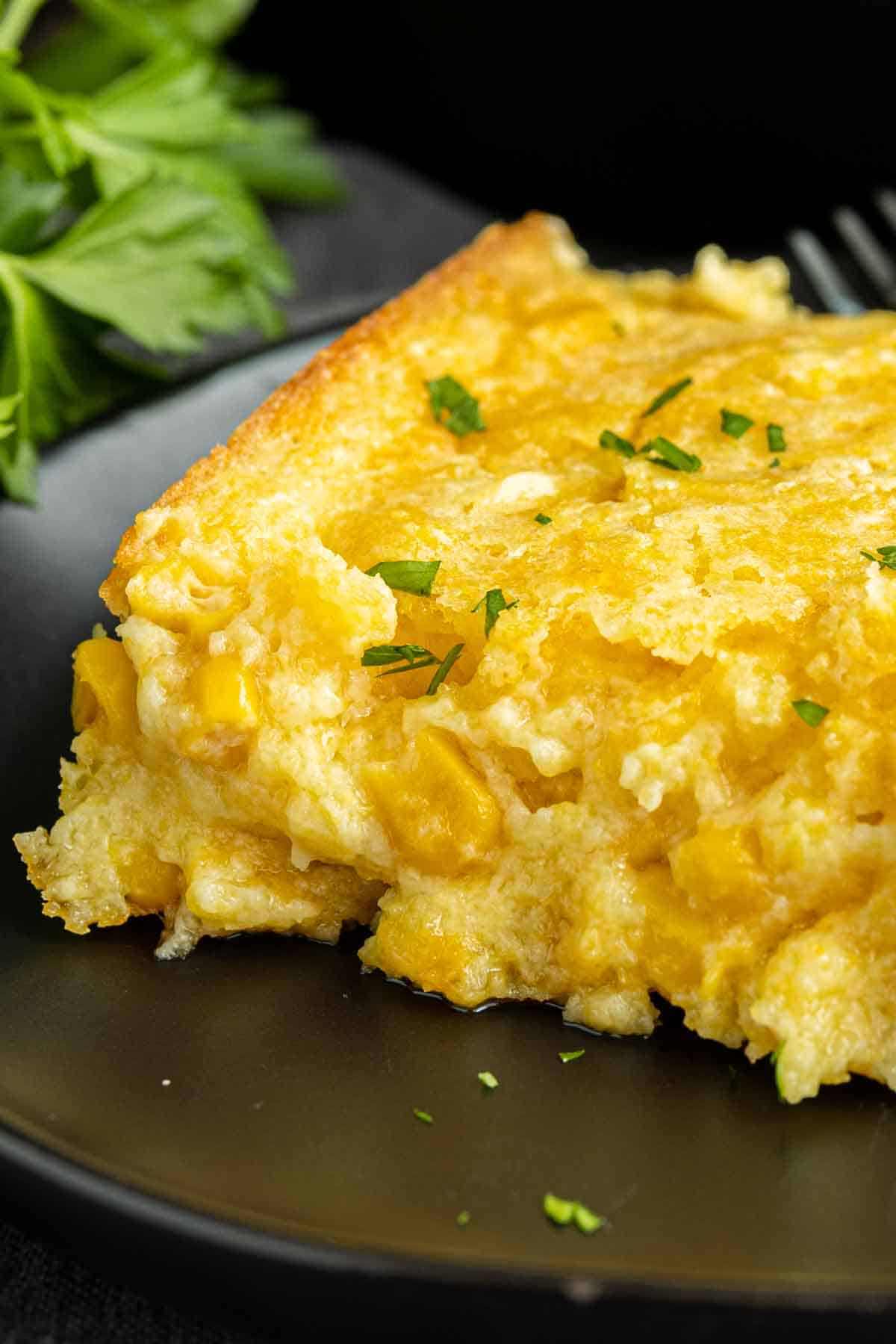 Creamed Corn Casserole on a black plate garnished with parsley