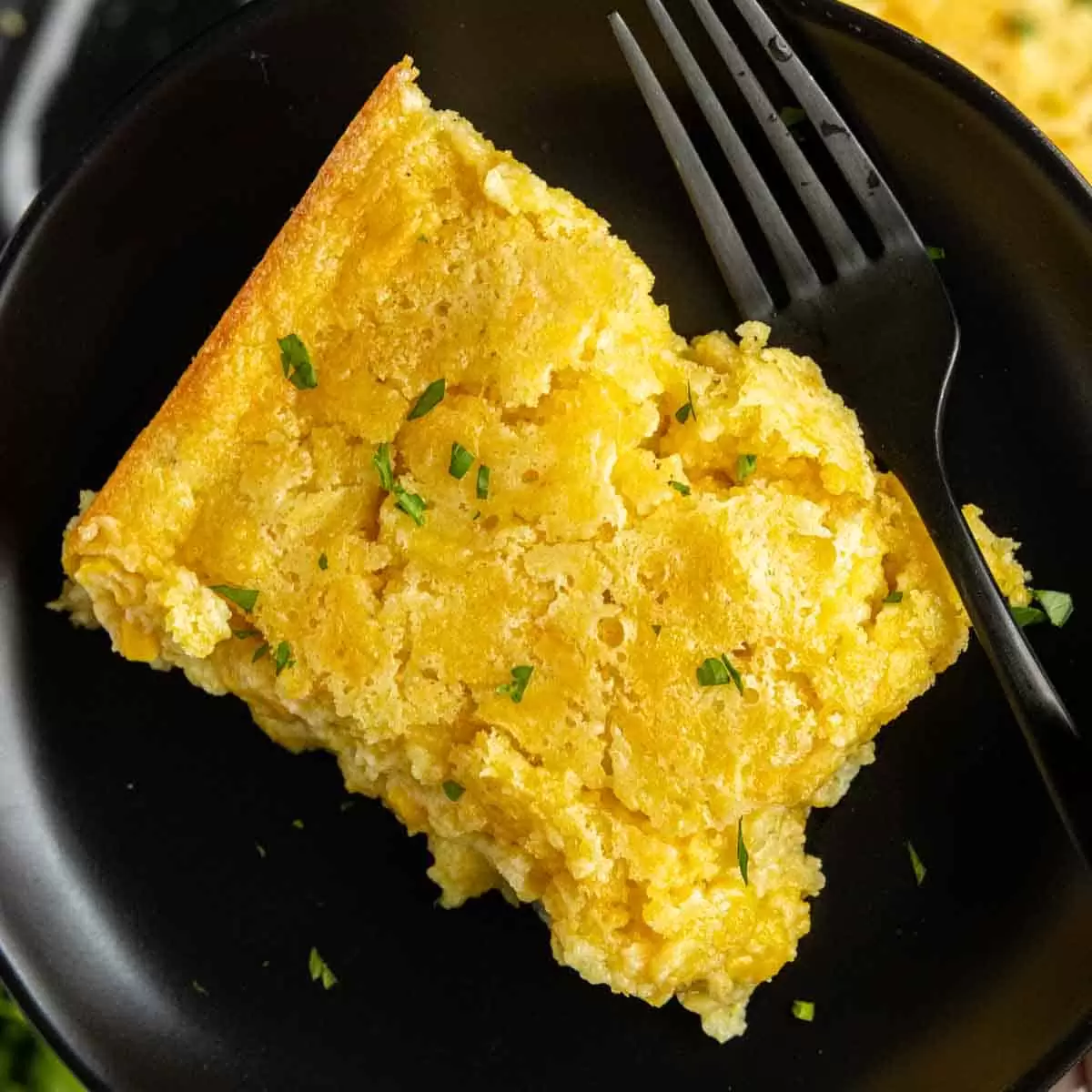 holding a plate of Creamed Corn Casserole with a black fork