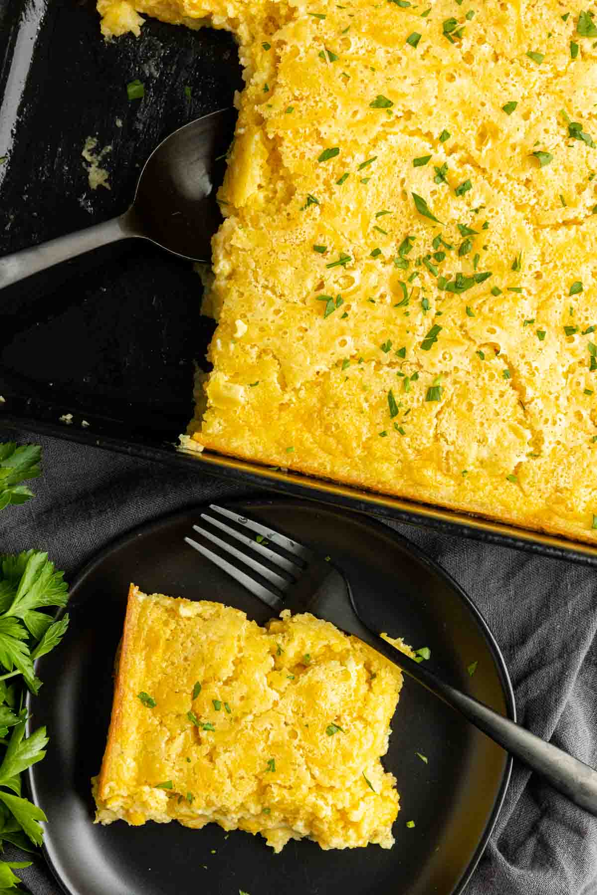 Creamed Corn Casserole on a black plate with black fork and casserole pan with spoon