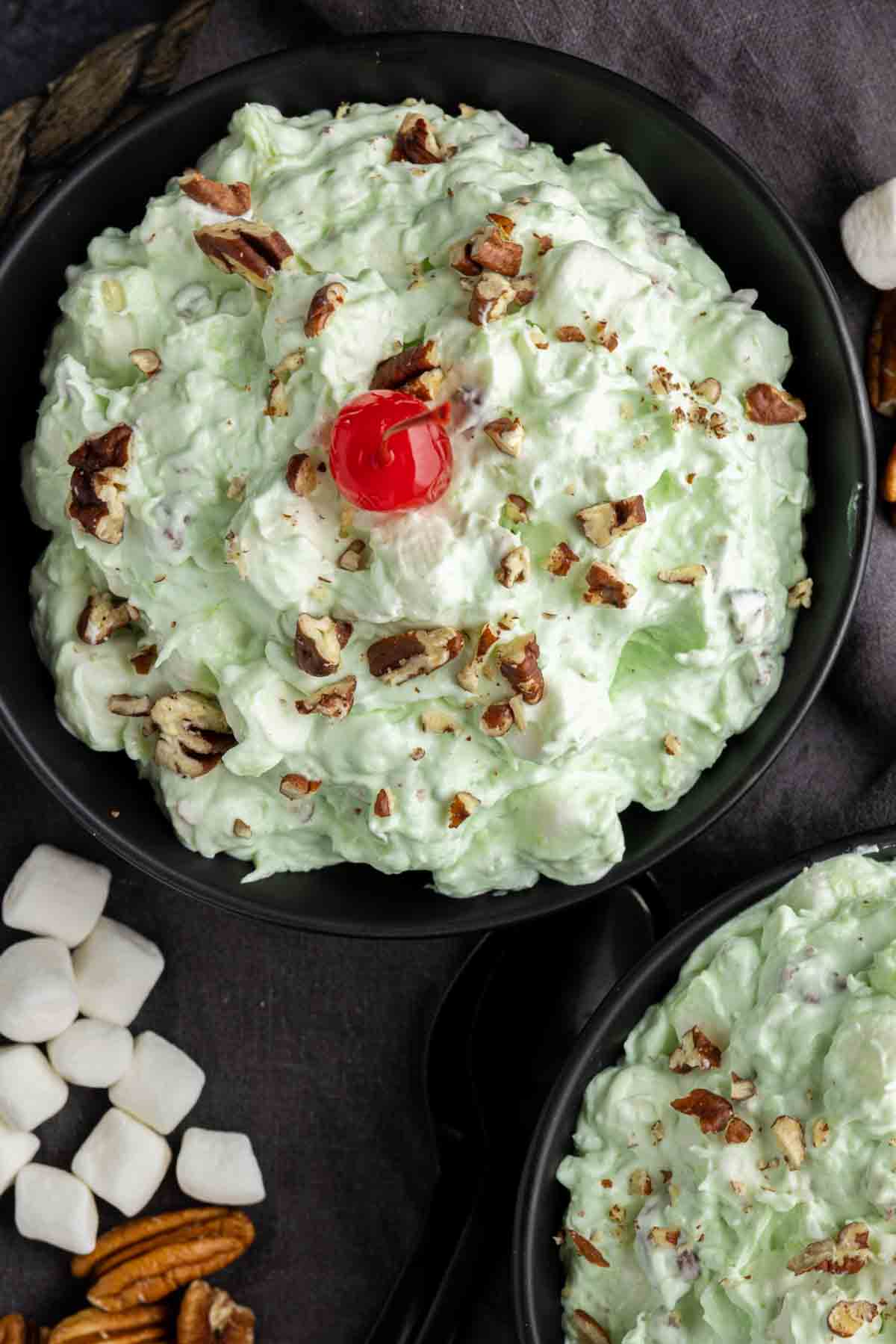 Watergate Salad in a bowl topped with chopped pecans and a cherry