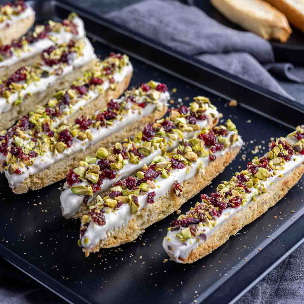 white chocolate dipped almond biscotti with cranberries and pistachios on a black sheet pan