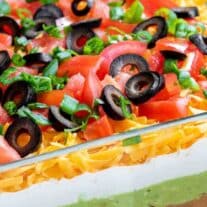 Guacamole dip in a baking dish with black olives and tomatoes.