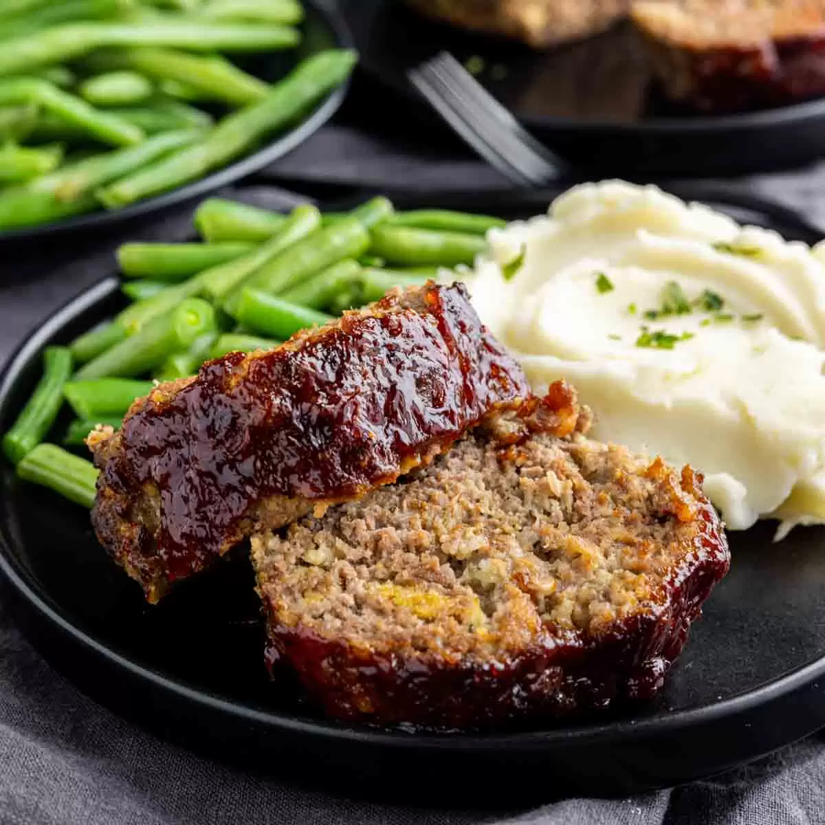 a black plate with Air Fryer Meatloaf, mashed potatoes and green beans