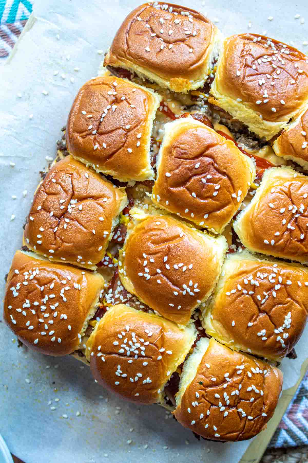 Bacon Cheeseburger Sliders topped with butter and sesame seeds