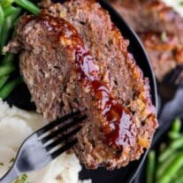 Meatloaf on a plate with mashed potatoes and green beans.