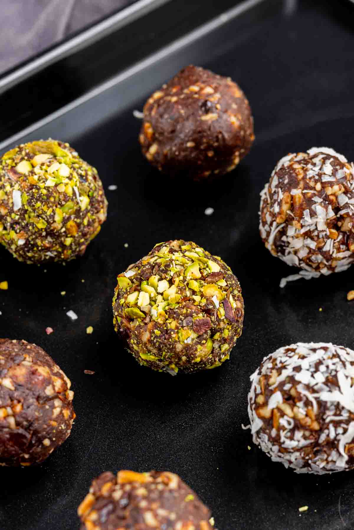 date balls rolled in chopped pistachios on a sheet pan