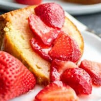 slice of Sour Cream Pound Cake on a plate with fresh cut strawberries