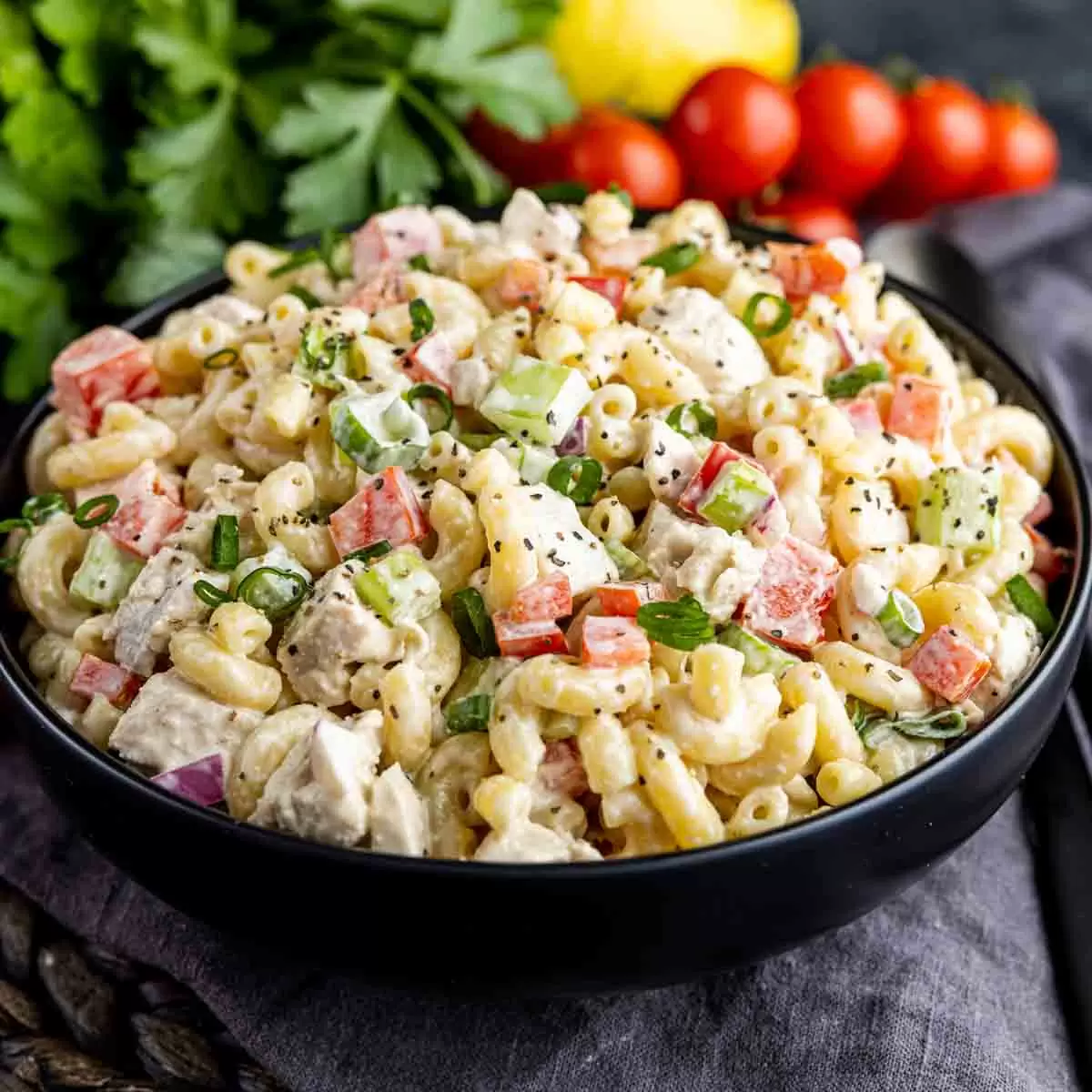 Chicken Macaroni Salad in a black bowl with parsley and tomatoes in background