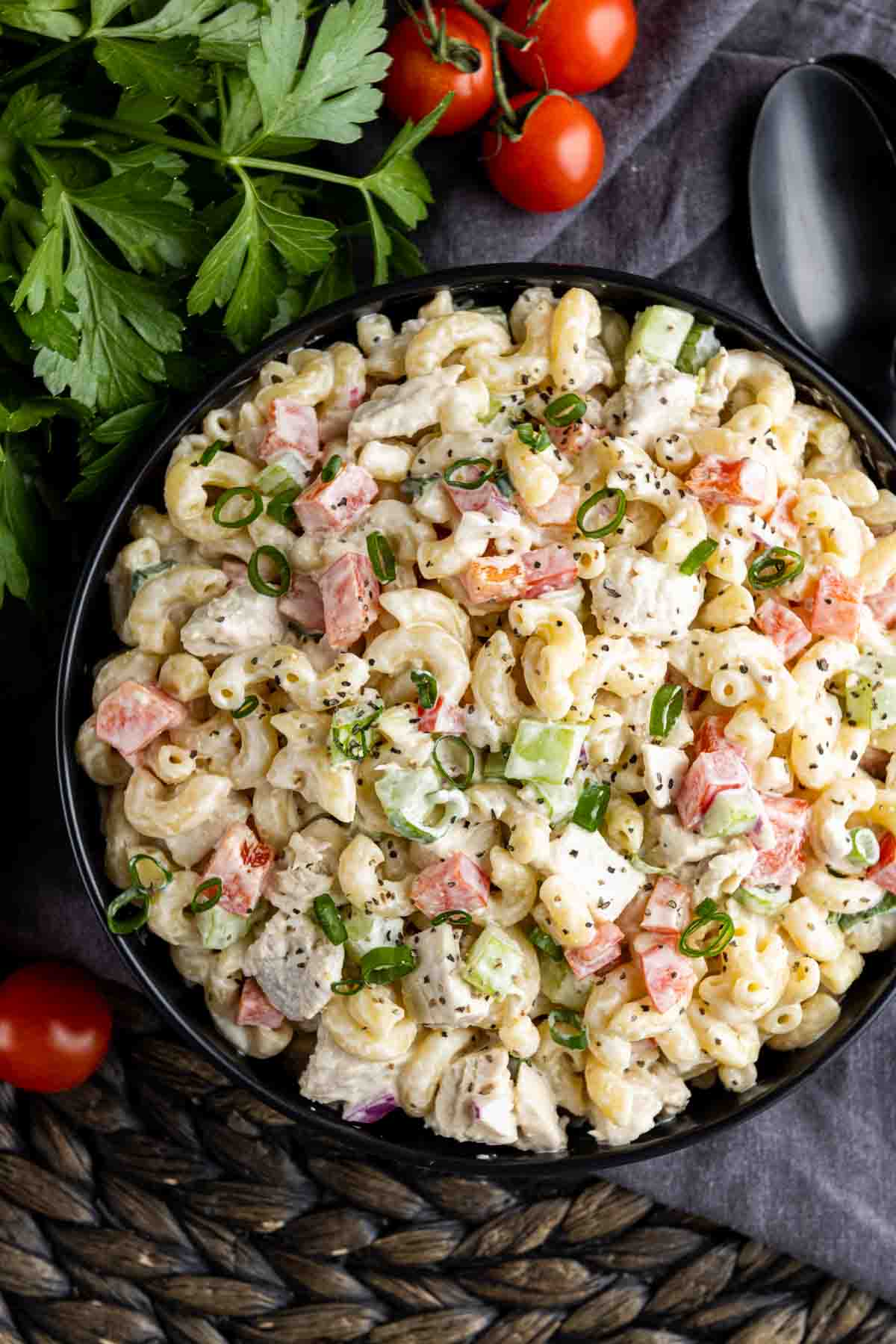 black bowl of Chicken Macaroni Salad with parsley and cherry tomatoes