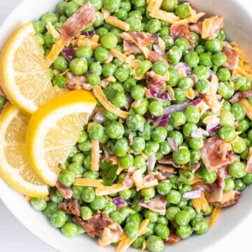 a white bowl of english pea salad garnished with fresh lemon slices