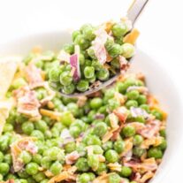 A bowl of pea salad with onions and bacon, with a spoonful being lifted out.