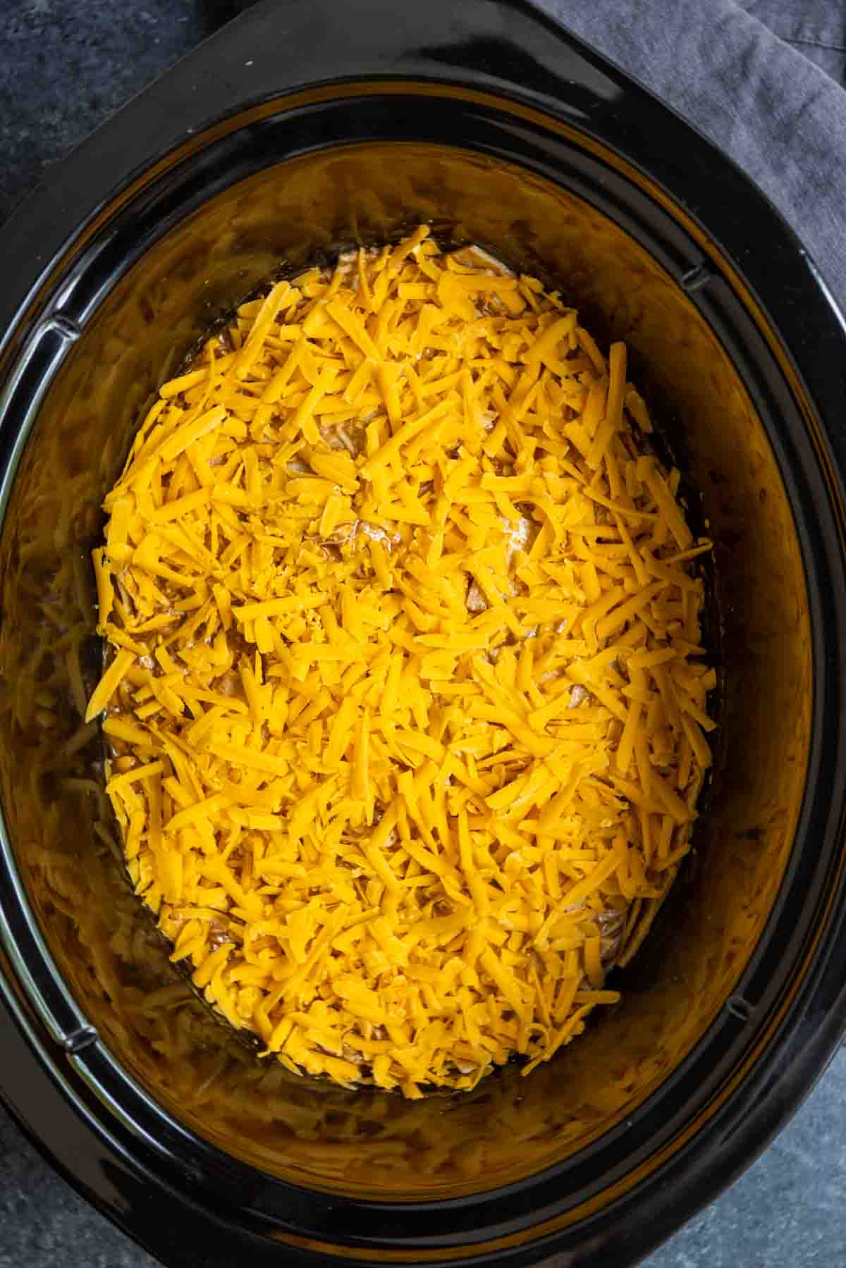 topping Crock Pot Chicken Enchiladas with shredded cheddar cheese