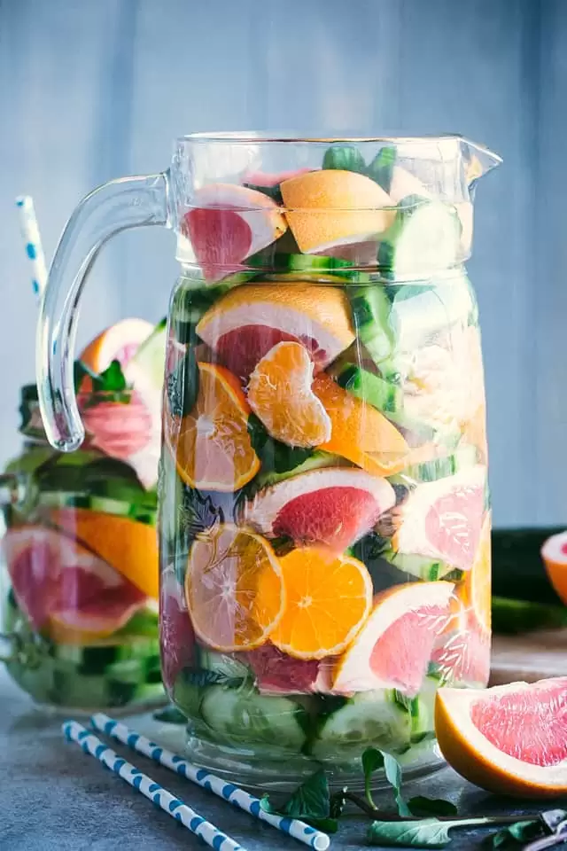 Large glass pitcher filled with water and fresh grapefruit, cucumbers and oranges.