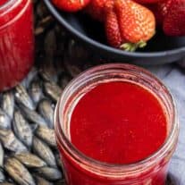 jar of Strawberry Coulis with a bowl of strawberries