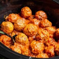 Crock pot meatballs in tomato sauce with a spoon.