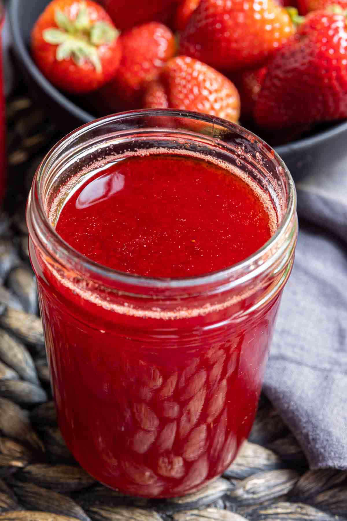 Strawberry Coulis in a glass jar with a bowl of strawberries in background