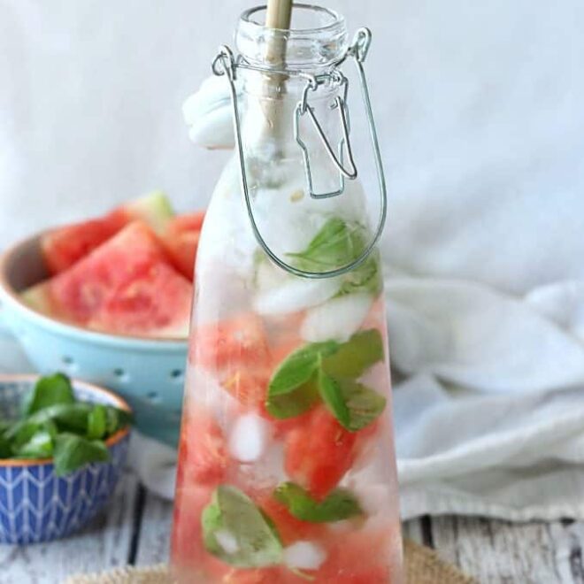 Glass bottle filled with ice, basil, and watermelon