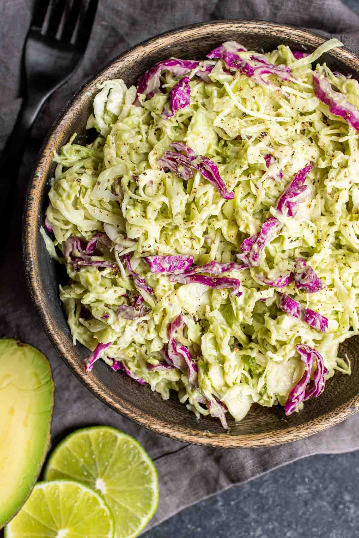 wooden bowl with Avocado Keto Coleslaw and black fork with lime slices and gray cloth