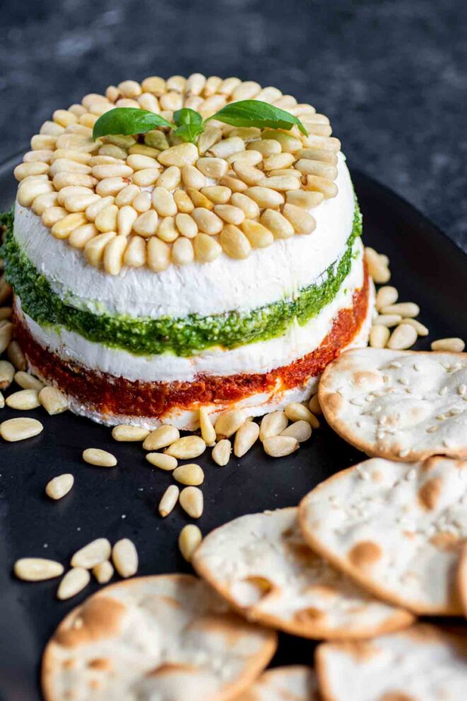 Pesto Cream Cheese Spread on a blacl platter with pine nuts and crackers