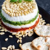 Pesto Cream Cheese Spread on a blacl platter with pine nuts and crackers
