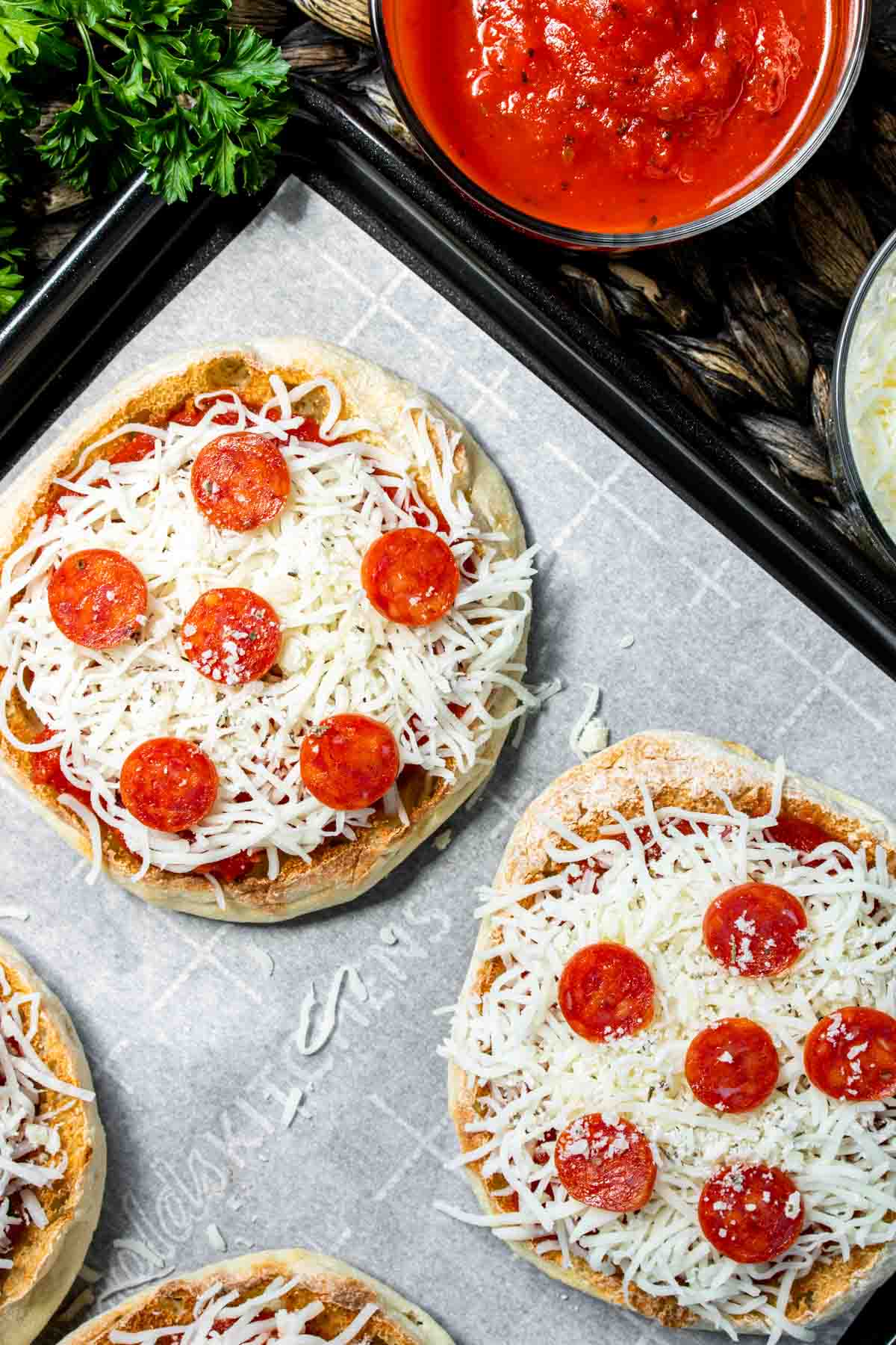 english muffin pizzas on a baking sheet with toppings on them.