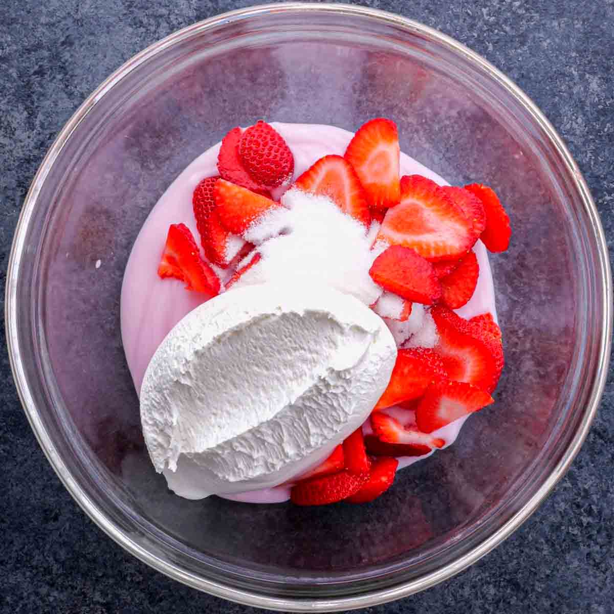 A bowl of strawberry yogurt with whipped cream and strawberries.