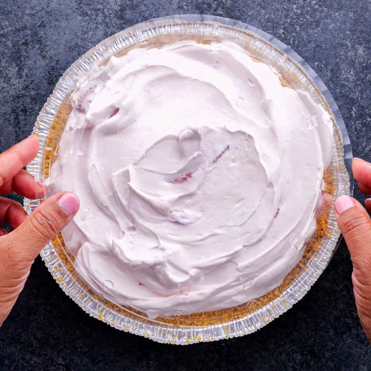 A person holding a pie with strawberry filling top.