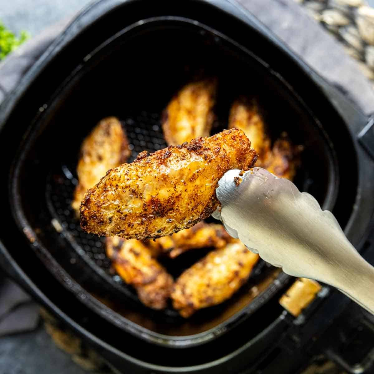 Frozen Chicken Wings in the Air Fryer in an air fryer with tongs