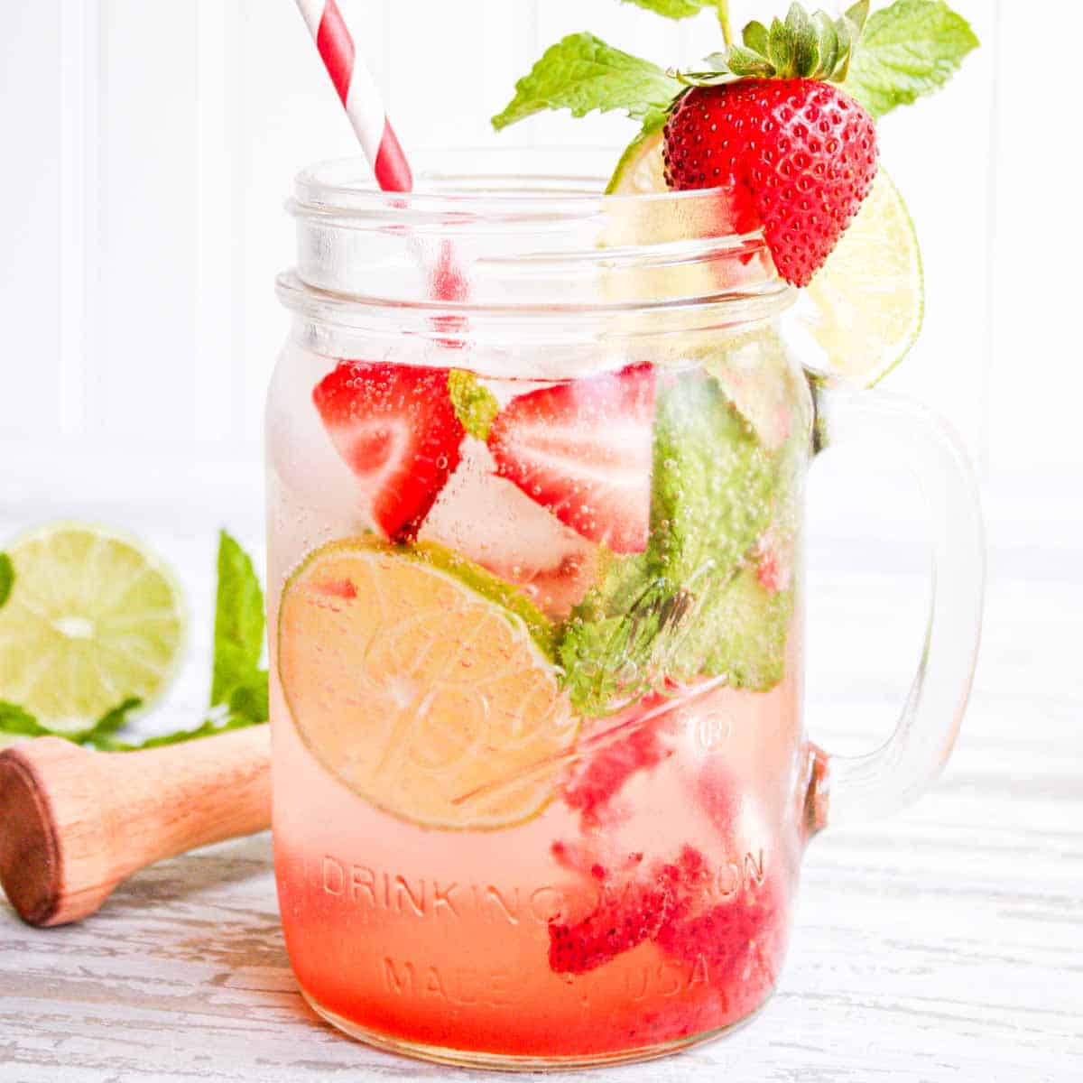 Strawberry lemonade in a mason jar with limes and strawberries.