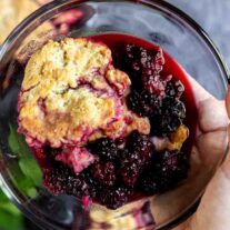 holding a bowl of easy blackberry cobbler with blackberrys in focus