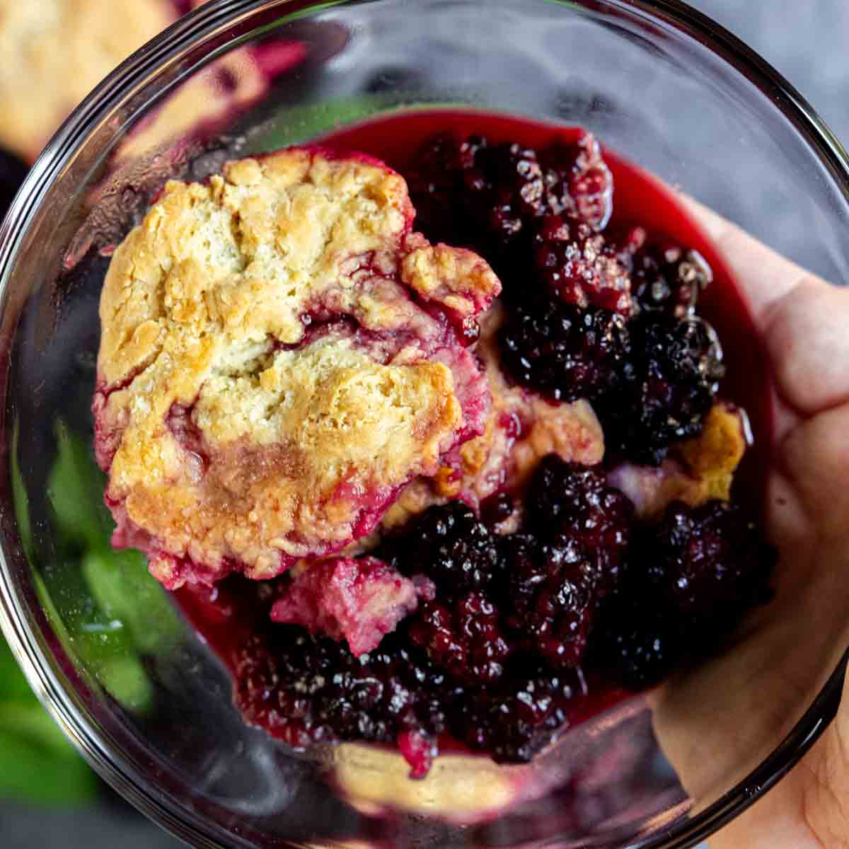 holding a bowl of easy blackberry cobbler with dough in focus