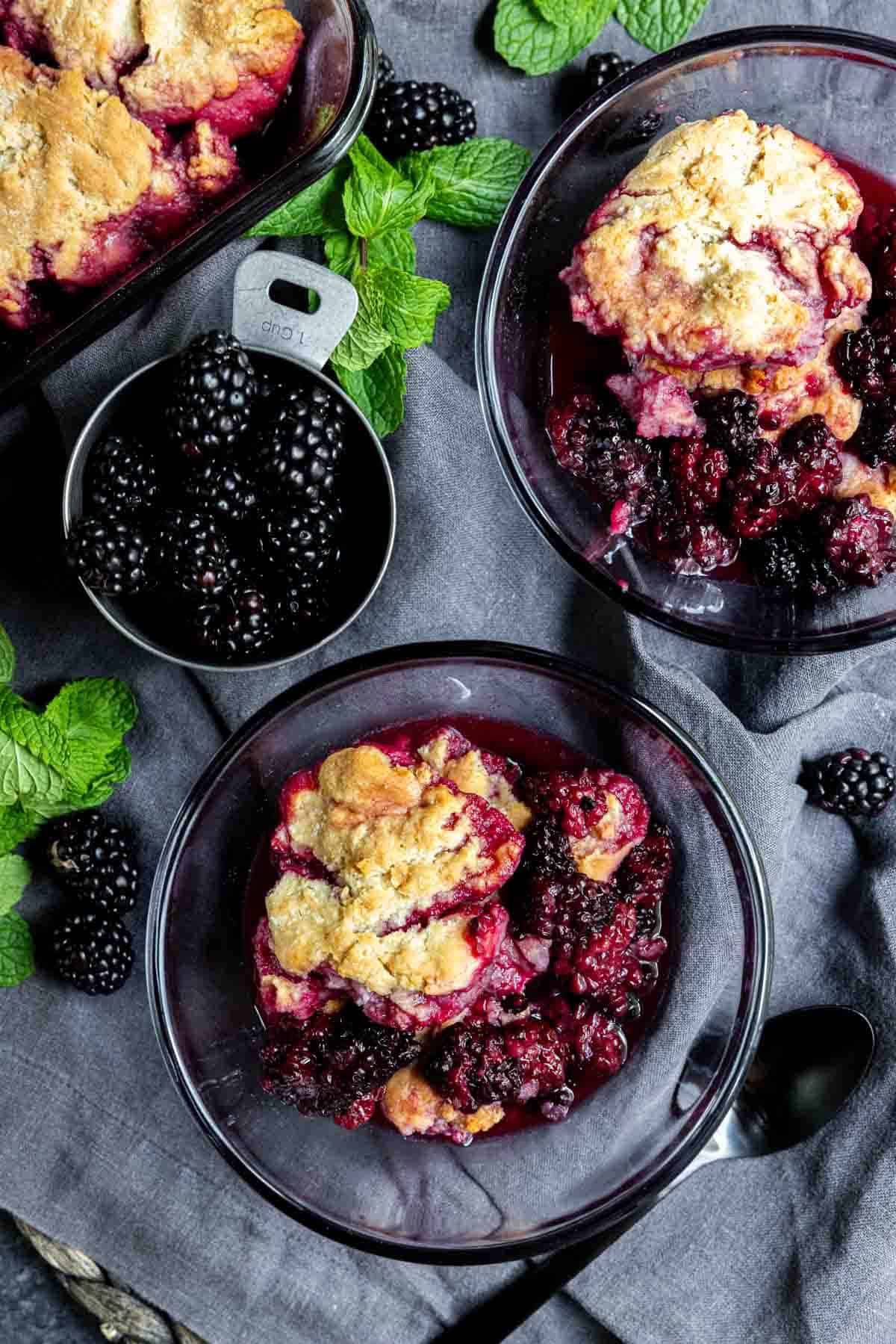 easy blackberry cobbler in two bowls with a cup of fresh blackberrys and fresh mint