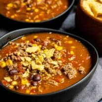Two bowls of mexican chili soup on a gray background.
