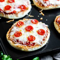 A tray of english muffin pizzas on a baking sheet.