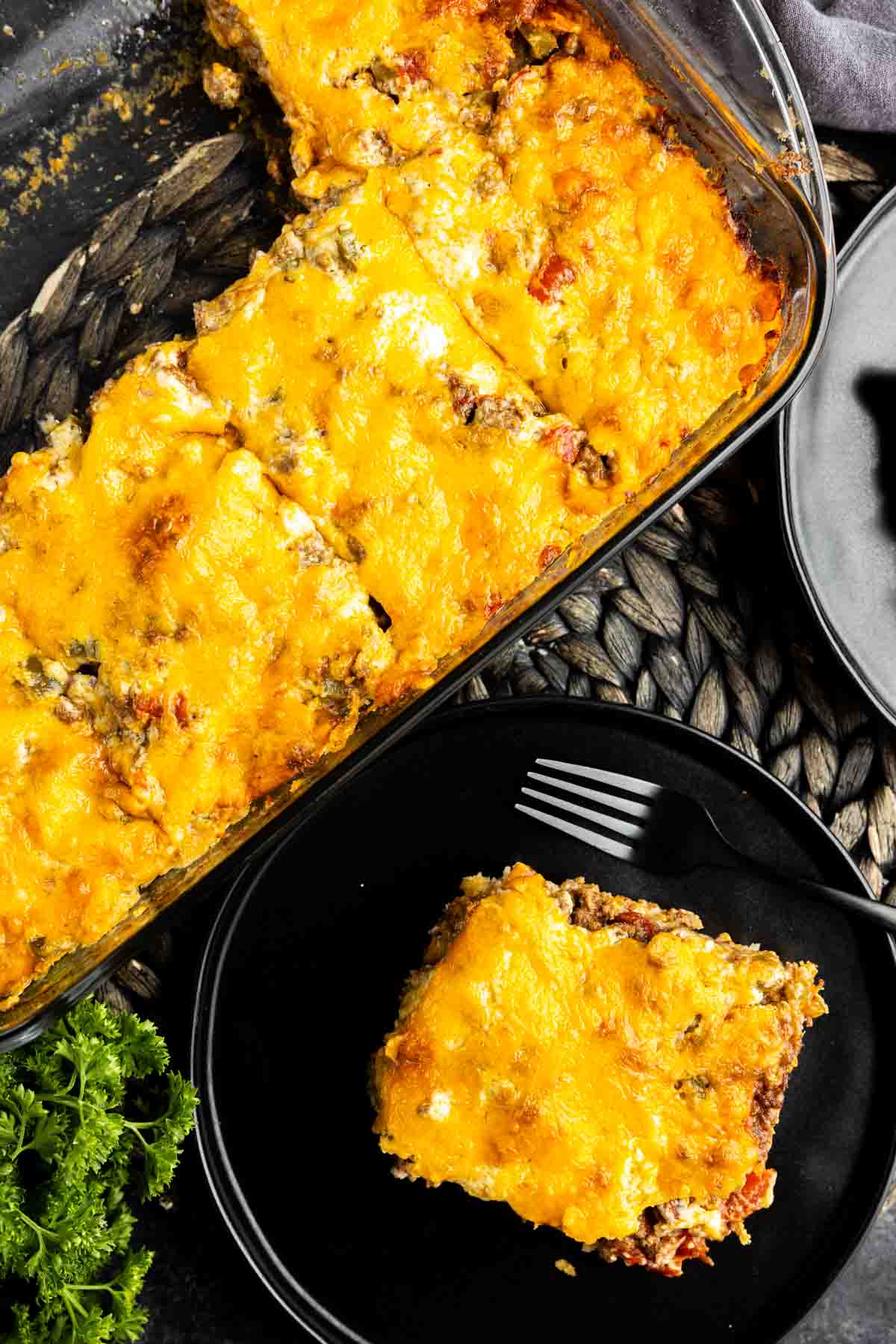 A casserole dish with a slice of John Wayne Casserole on a plate and a fork.