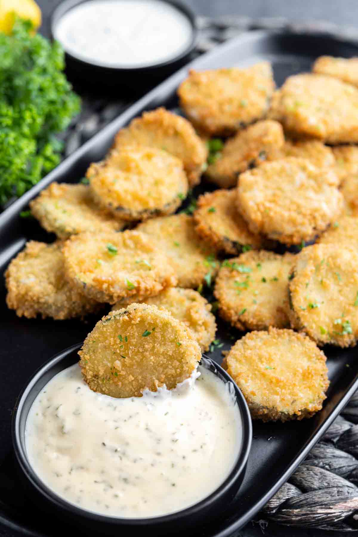 Fried zucchini with aioli sauce on a black plate.